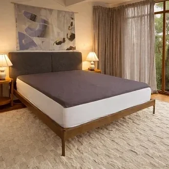 A grounding sheet fitted on a bed in a warm, lamp-lit bedroom